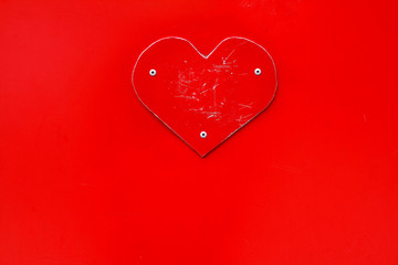 Scratched red metal heart on red background