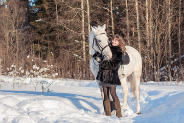 Nice girl and white horse in a forest in a winter