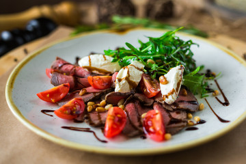 On a plate, on a wooden surface, close-up roast beef salad with rocket salad, cherry tomatoes,...