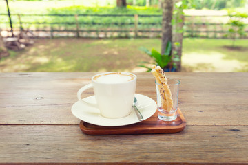 Coffee cup and pastry on wooden table with nature background.