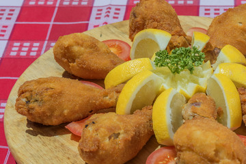 fried chicken legs arranged on wooden plate with parsley lemon tomato