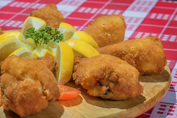 fried chicken legs arranged on wooden plate with parsley lemon tomato