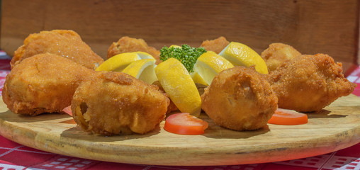 fried chicken legs arranged on wooden plate with parsley lemon tomato