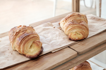 Baked butter croissant on paper on wooden tray in cafe bakery shop. Closeup view