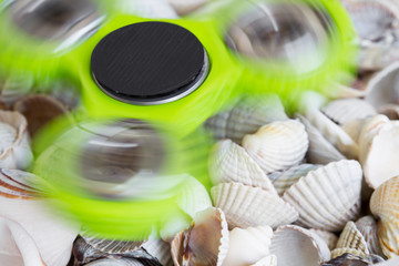 Fidget spinner is rotating on sea shells. Closeup. Selective focus.