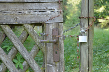 Neues Vorhängeschloss an einer alten, verrosteten Kette und einem alten, mit Stacheldraht umwickelten Tor