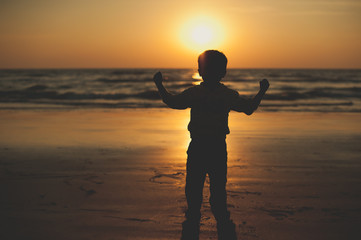 Child at sunset by the sea. Silhouette of a child on the beach. Little boy having fun on the beach. Sunset on sea. Silhouette of people