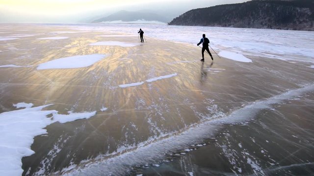 Two men are skating on the ice of frozen Lake Baikal during beautiful sunset.
