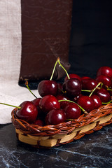 Fresh organic cherry in yellow wooden basket on dark marble background.