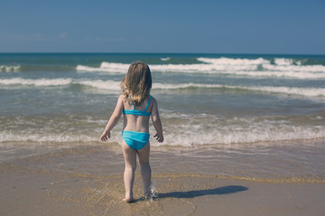 Vacation on the sea. Back view of pretty little girl on the sand beach.