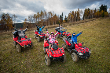 Young people in winter clothes with raised hands up on red atv off-road vehicles on a countryside trail in nature under the sky with clouds. Top view