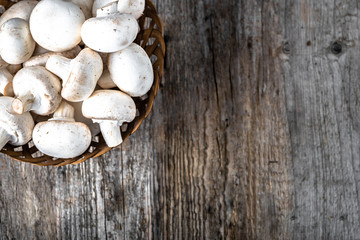 Fresh champignon mushrooms in a basket on wooden table, overhead