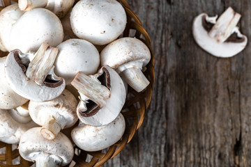 Fresh champignon mushrooms in a basket on wooden table, overhead
