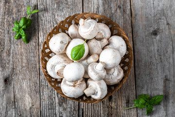 Fresh champignon mushrooms in a basket on wooden table, overhead