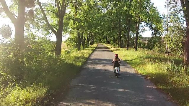 A girl is riding a moped on an alley with trees