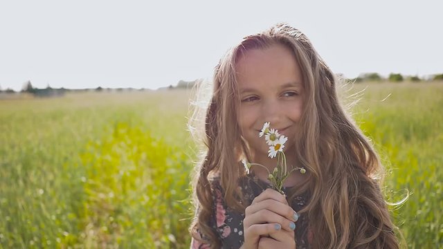 Little girl smelling a daisy spring flower in meadow field