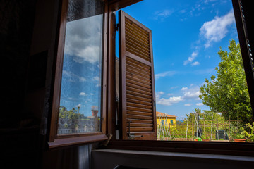 Window with open wooden shutters on the garden reflecting in the glass