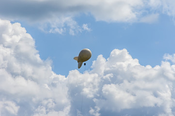 White airship of a soft system with stabilizers and a motor hovers in the sky © IKvyatkovskaya