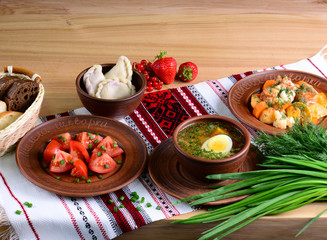 Traditional national food of Ukraine: vegetable soup with boiled egg, salad with tomatoes in sunflower oil, vareniki with berries, vegetable stew on a tablecloth with ornament. Original feed.