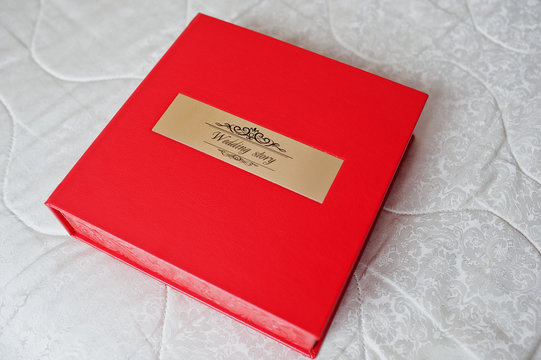 Sohisticated red leather wedding photobook or photo album with golden inscription laying on the sofa.