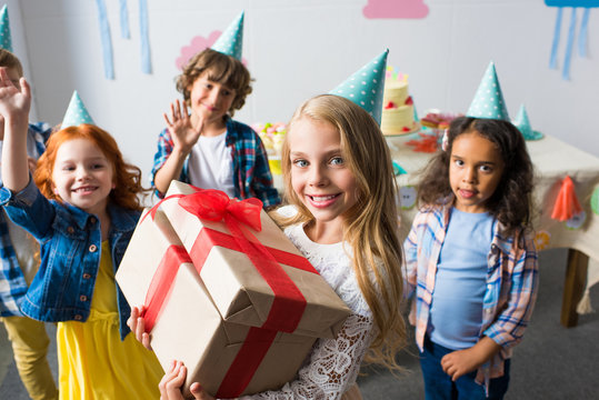 adorable smiling girl holding birthday presents while friends waving hands