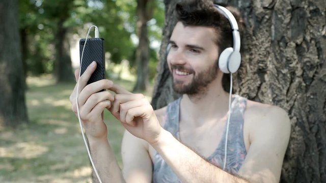 Handsome man looks happy while listening music and doing selfies on smartphone, steadycam shot
