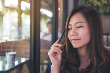 Closeup portrait image of a beautiful Asian woman closing her eyes and sitting in modern cafe while thinking about business and study