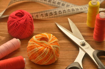 Sewing scissors among balls and spools of threads with meter on the wooden table