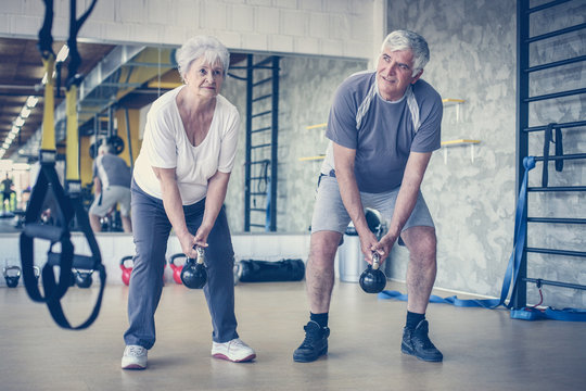 Senior Couple Workout In Gym. Senior People Lift Weight.