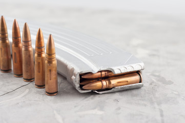 Silver full magazine for assault rifle and row of bullets on old grey broken concrete