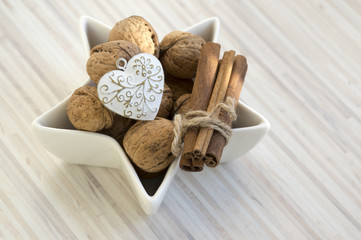 Healthy eating, various nuts in a white bowl, star shaped, wooden table, Christmas decoration in the kitchen, Variety of nuts: hazelnuts, walnuts, fresh raw cinnamon bark, heart christmas ornament