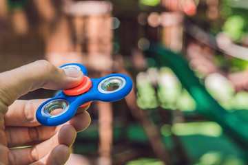 Boy playing with fidget spinner. Child spinning spinner on the playground. Blurred background