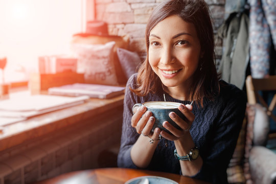 A beautiful asian woman drinking hot coffee or tea from vintage cup in modern loft cafe