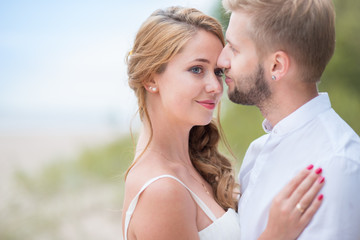 Young happy just married couple walking holding hands on the beach along the sea on summer evening