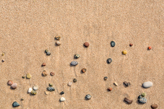 Summer view of small round pebbles on sunny beach, seen from above.