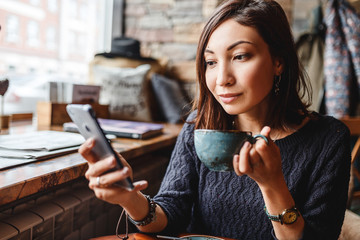Young charming asian woman calling with cell phone while sitting alone in coffee shop