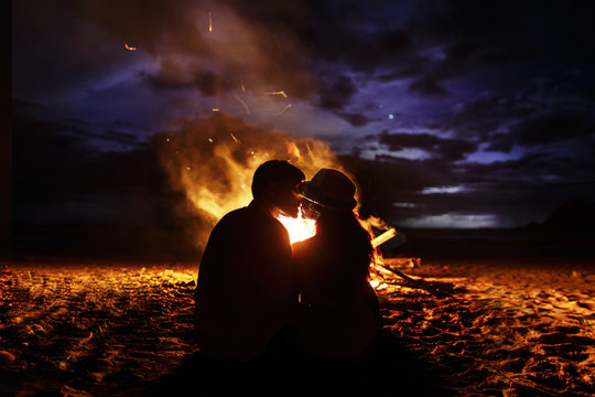 Kissing couple sits before a fireplace on the beach