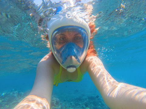 Snorkeling in full face mask. Summer activity. Beautiful girl in shallow seawater.
