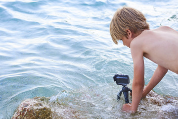 Fototapeta premium Child boy shooting movie with action outdoor waterproof camera in the sea