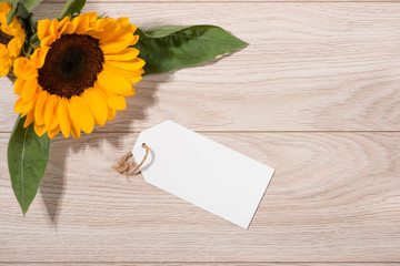 Blank white tag paper with color flowers on wooden background. Top view. Mock up