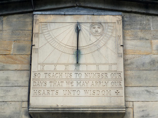 old sundial on a stone wall with inscription and carving of the sun with roman numerals
