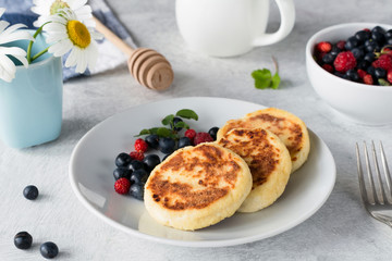 Syrniki, sierniki or cottage cheese pancakes served with honey and wild berries on white plate. Closeup view. Traditional Russian cuisine dish for breakfast or lunch