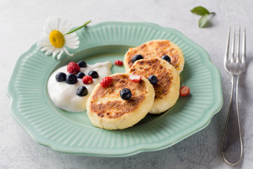 Syrniki, sierniki or cottage cheese pancakes served with sour cream and wild berries on vintage green plate. Closeup view. Traditional Russian cuisine dish for breakfast or lunch