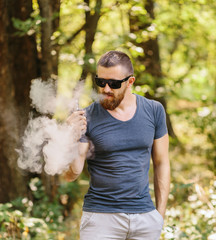 Young man with beard vaping an electronic cigarette outdoor. hipster smoke vaporizer.