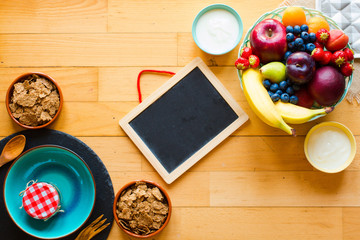 Bowl of fresh fruit with banana, apple, strawberries, apricots, blueberries, plums, whole grains, forks, top view