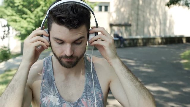 Handsome man in camis shirt connects headphones to smartphone and plays music, steadycam shot
