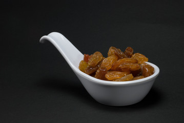 Raisins in a white spoon have a black background.