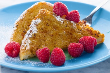 French toast with raspberries and honey served on sky blue plate and dessert fork