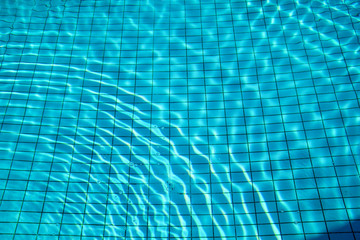 Blue ripped water in swimming pool. Swimming pool bottom caustics ripple and flow with waves background. Clear light blue pool water ripples with sun reflections. Surface of blue swimming pool.