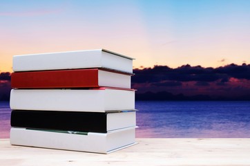 stack book on desk, no labels, blank spine with view of blurred beautiful twilight sky on the sea at sunset, education back to school and landscape nature concept, copy space